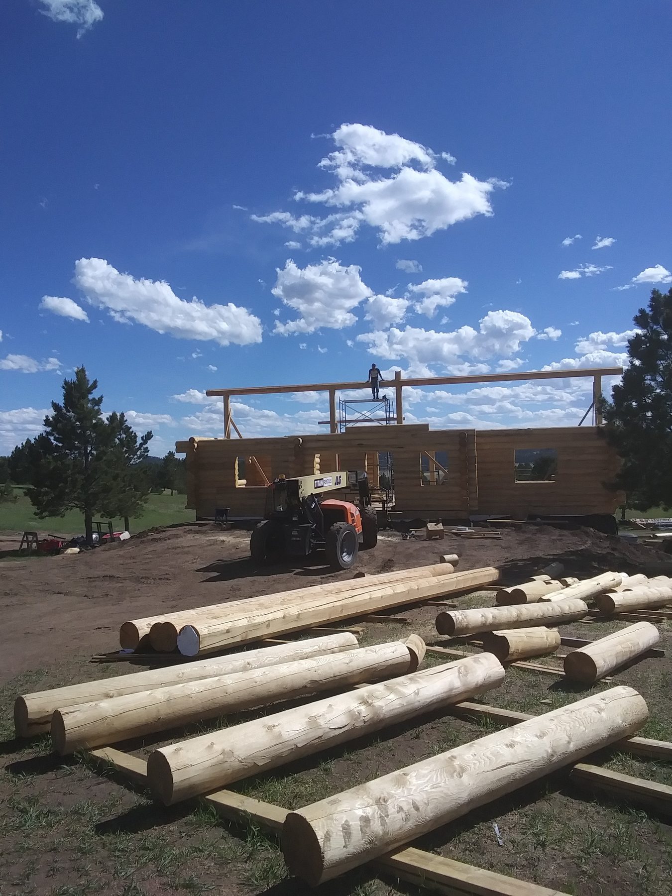 Milled logs stacked on the graded site, waiting to be set.