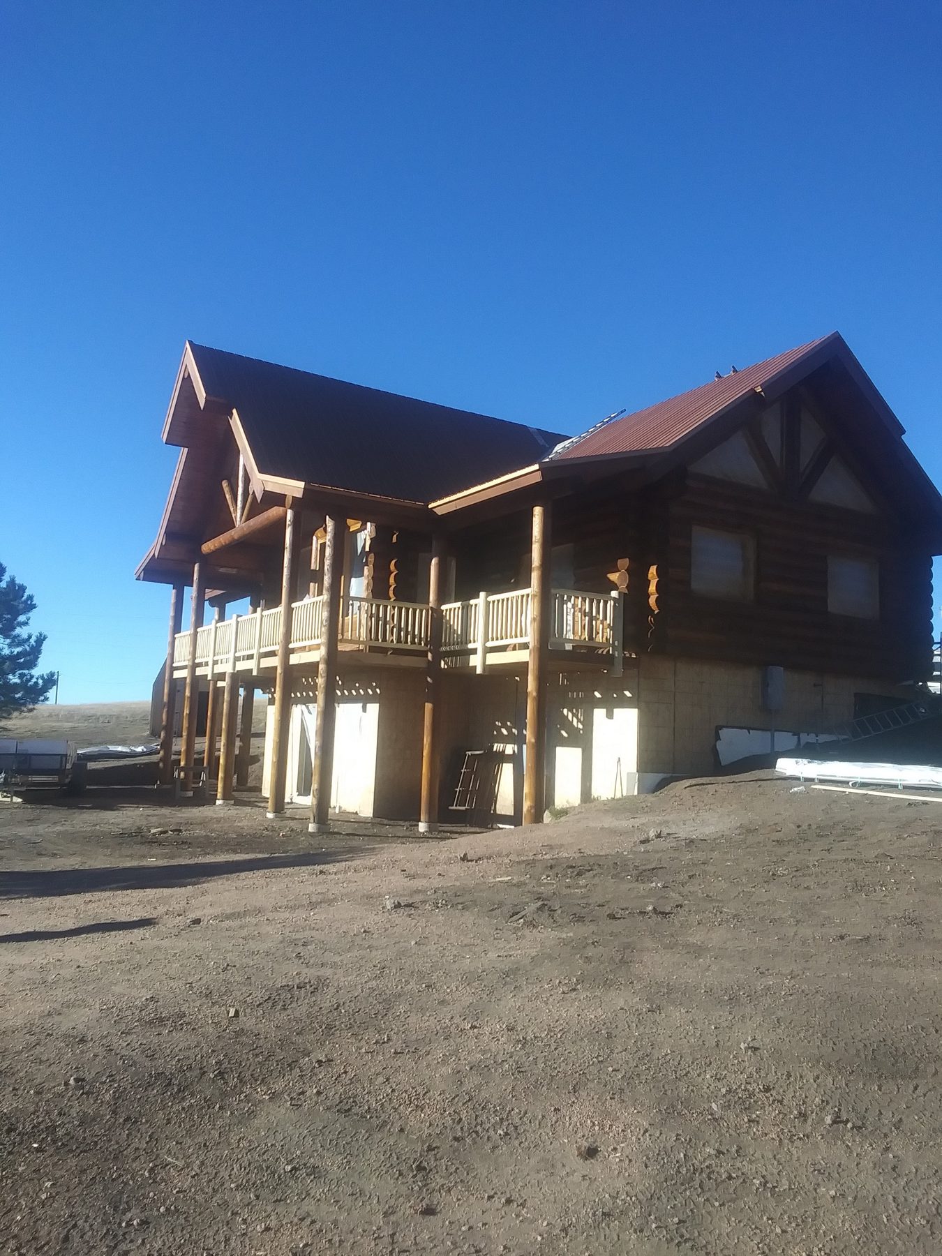 Exterior essentially complete: red metal roof, log walls, wraparound deck.