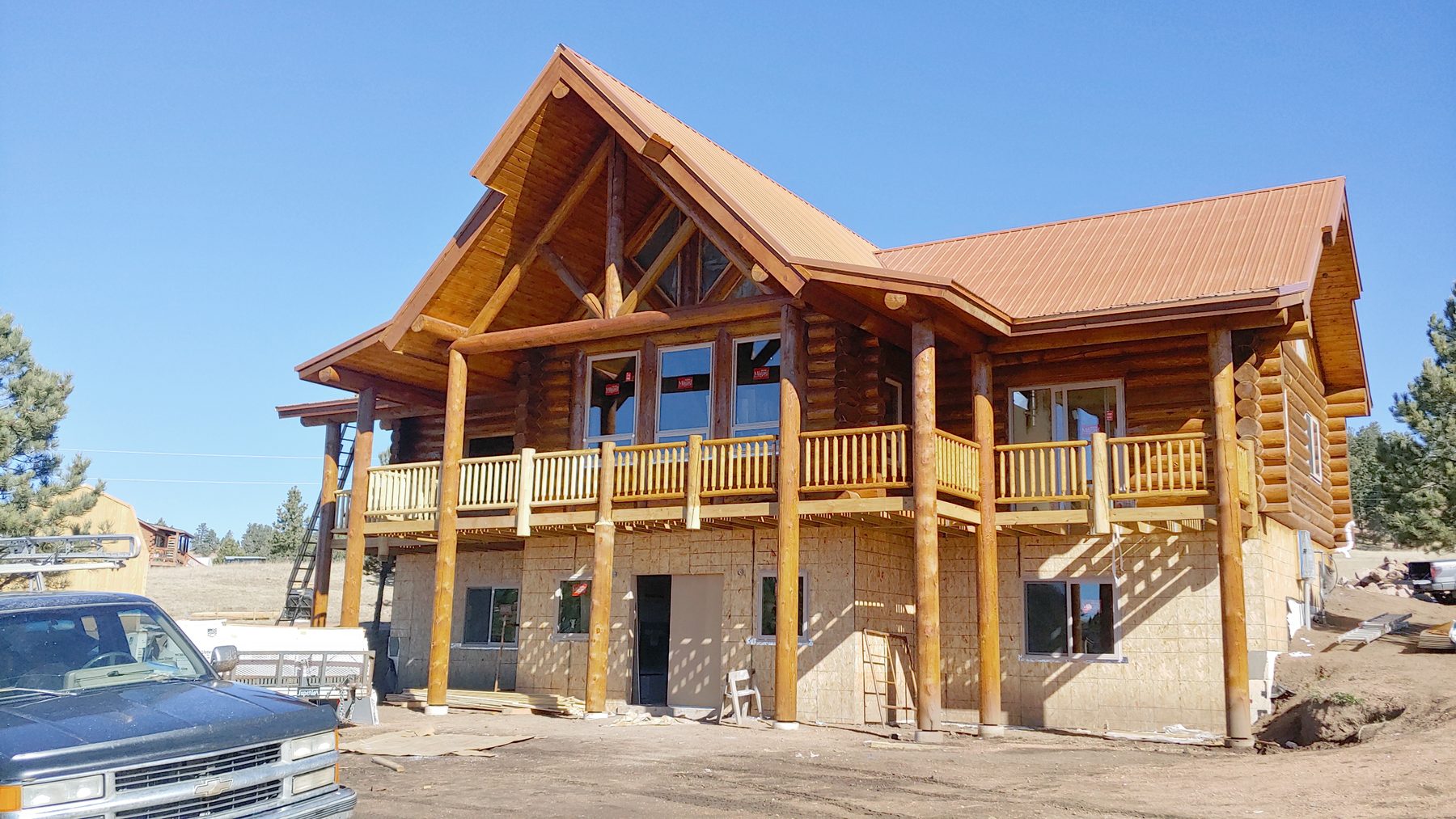 The completed log home: red roof, full-width deck, walkout level below.