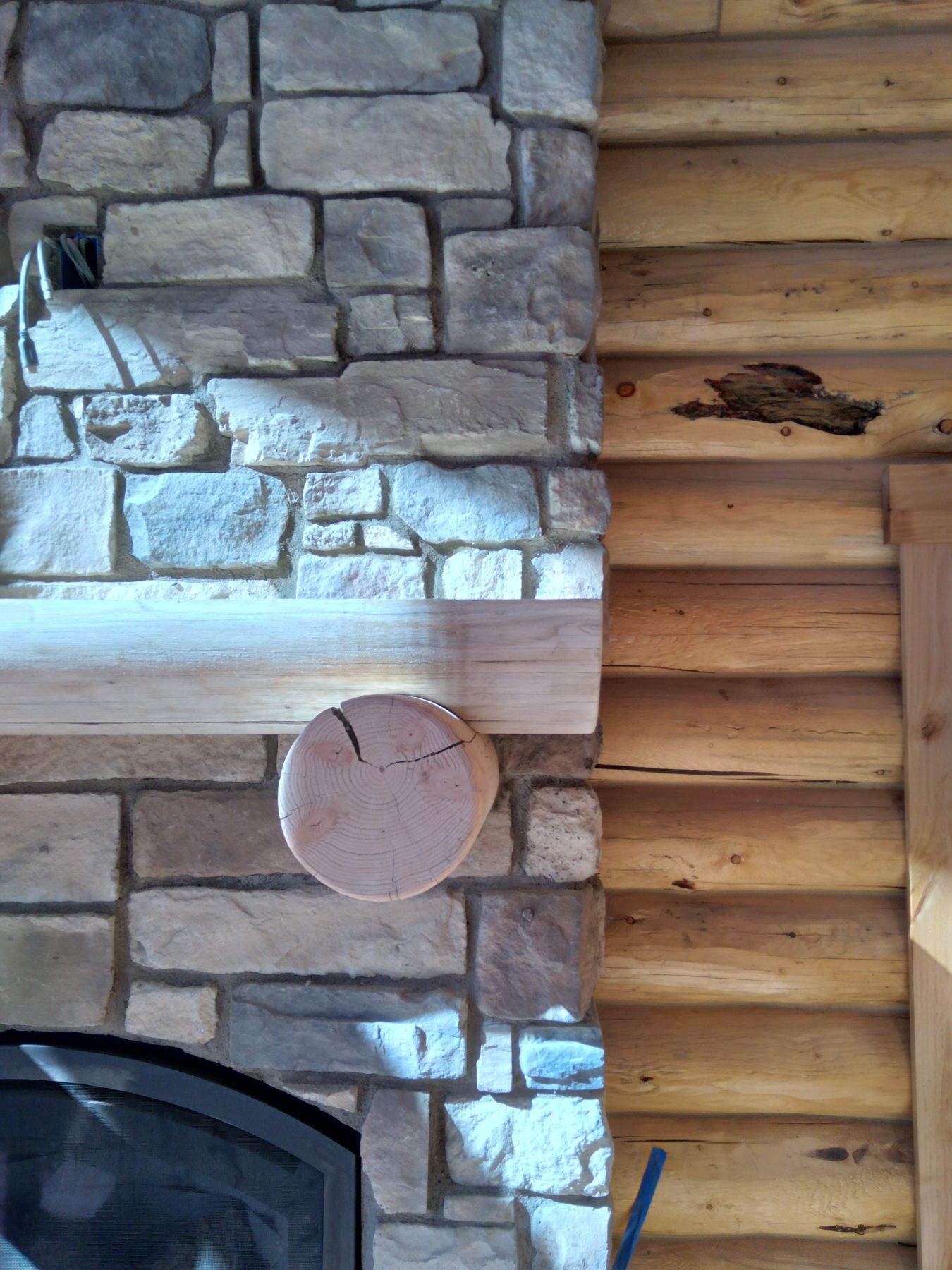 Stacked stone meeting the log wall beside the firebox.